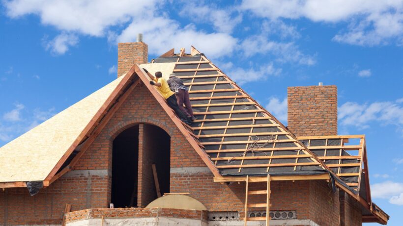 House under construction. Workesr installing fibreboard on the roof